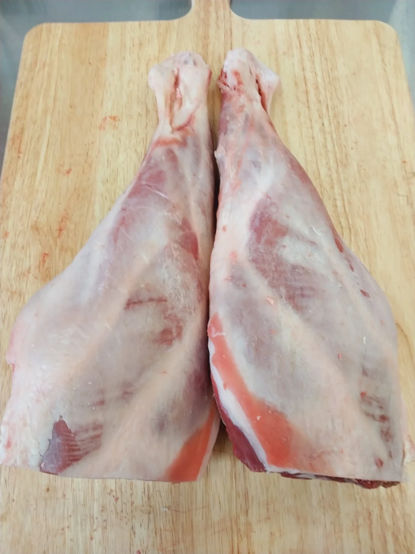 Two whole fresh halal lamb legs on a wooden cutting board