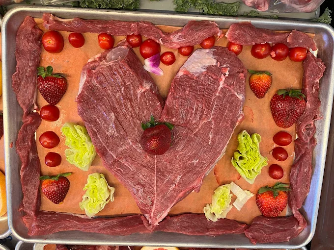 Halal flank steak cuts arranged in a heart shape with strawberries and tomatoes