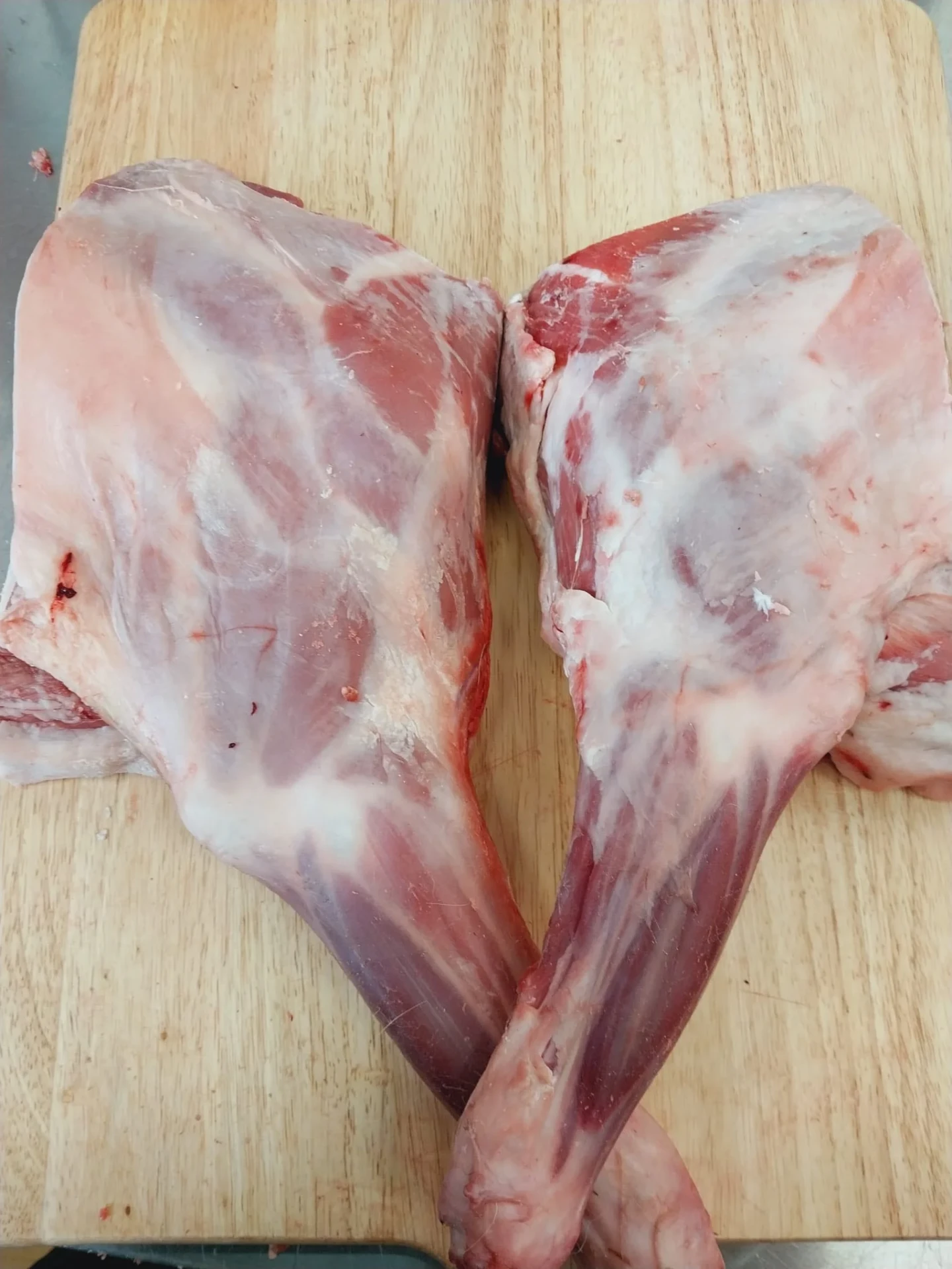 Two fresh halal lamb shoulders on a wooden cutting board