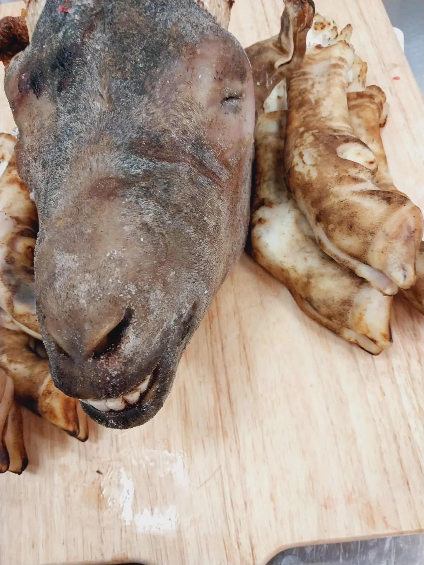 Whole singed brown halal goat head with goat feet on a wooden board