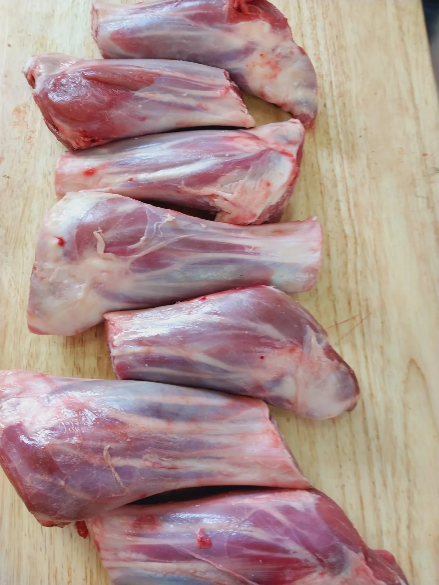 Fresh halal lamb shanks lined up on a wooden cutting board